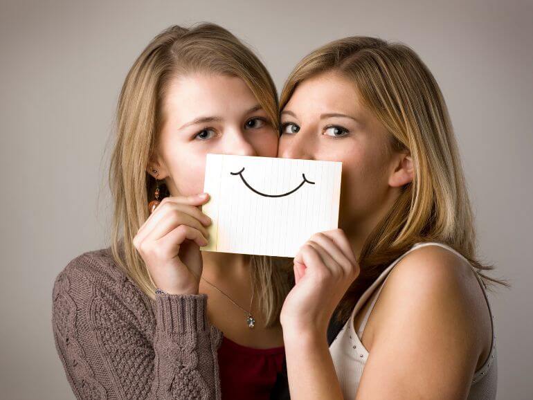 Két lány egy papírcetlin lévő mosolyt tart a szája elé .