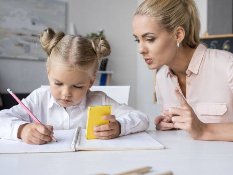 Zöld ceruza kockás füzetbe matek példákat ír.