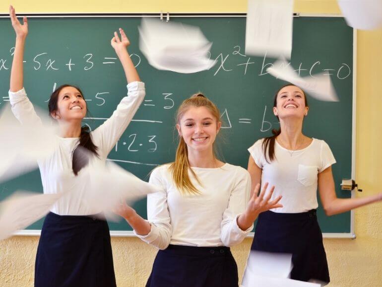 Három csinos, mosolygós lány, papírlapokat dobnak fel a levegőbe.
